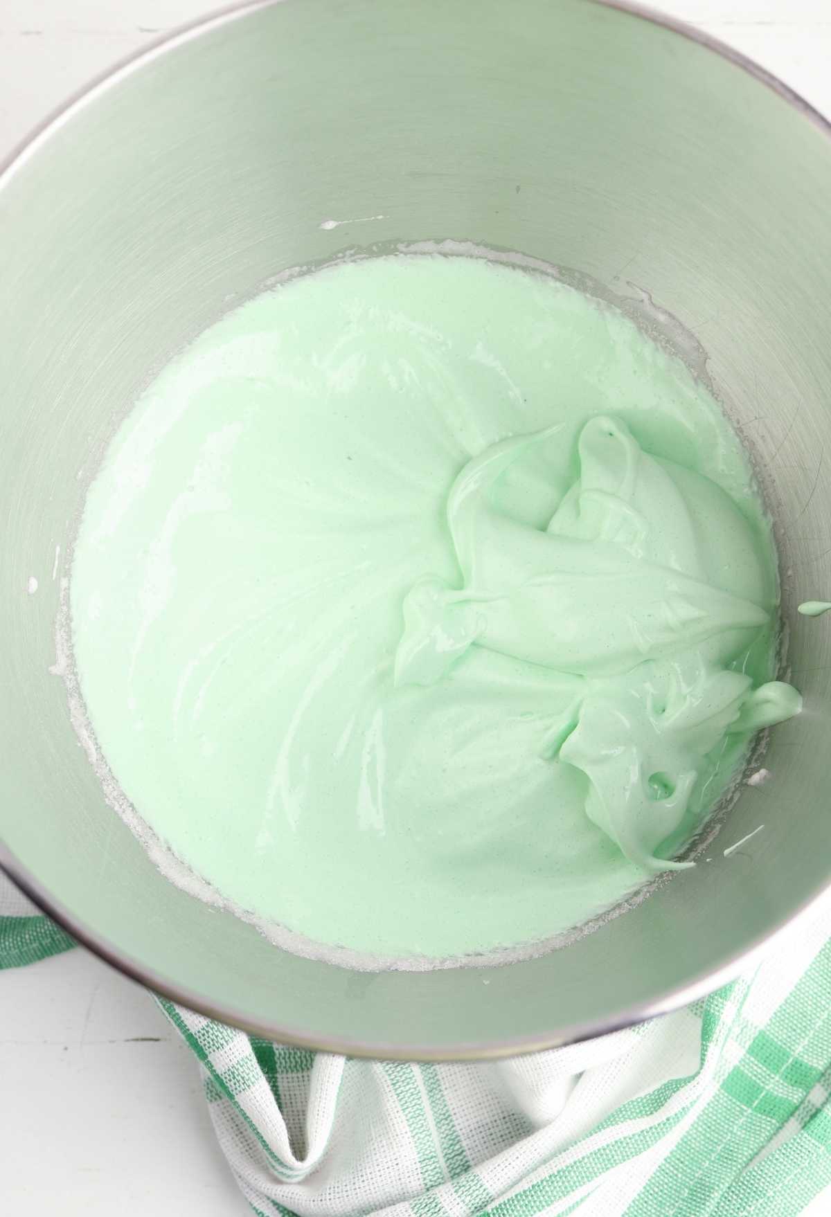 Green icing in a bowl on a table, perfect for Christmas Tree Meringue Cookies.