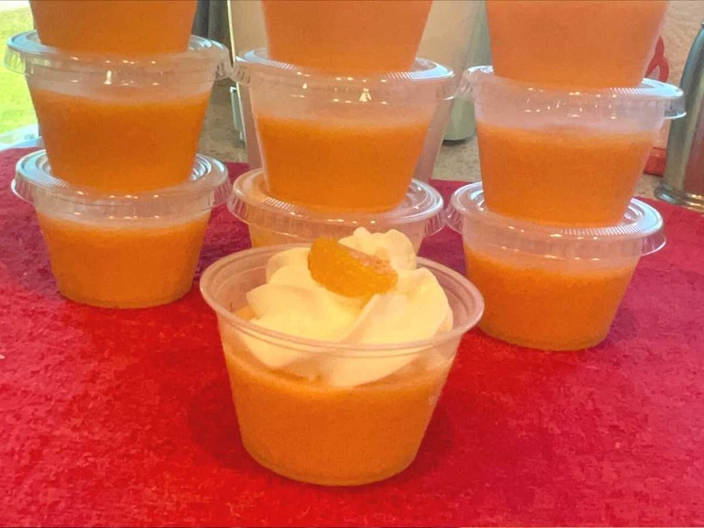 A tray of orange jello shots with whipped cream on top.