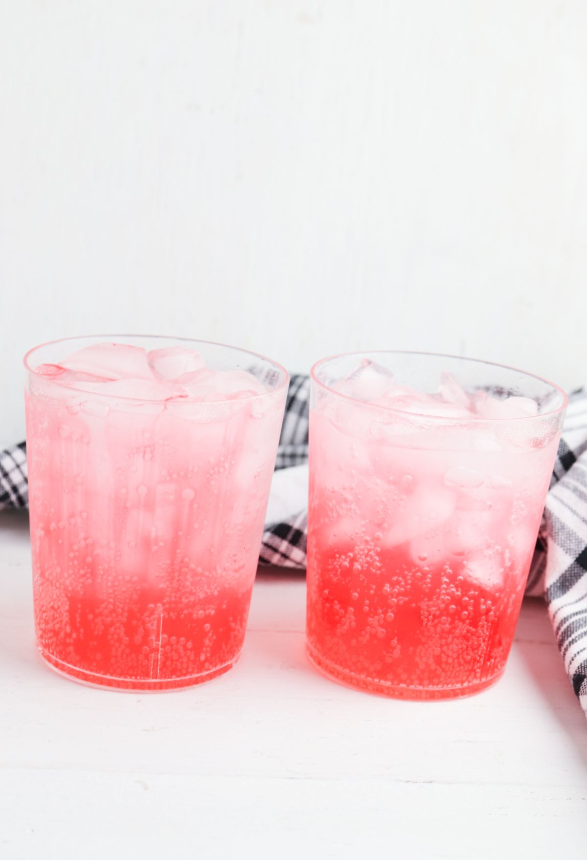 Two glasses of pink iced tea on a wooden table.