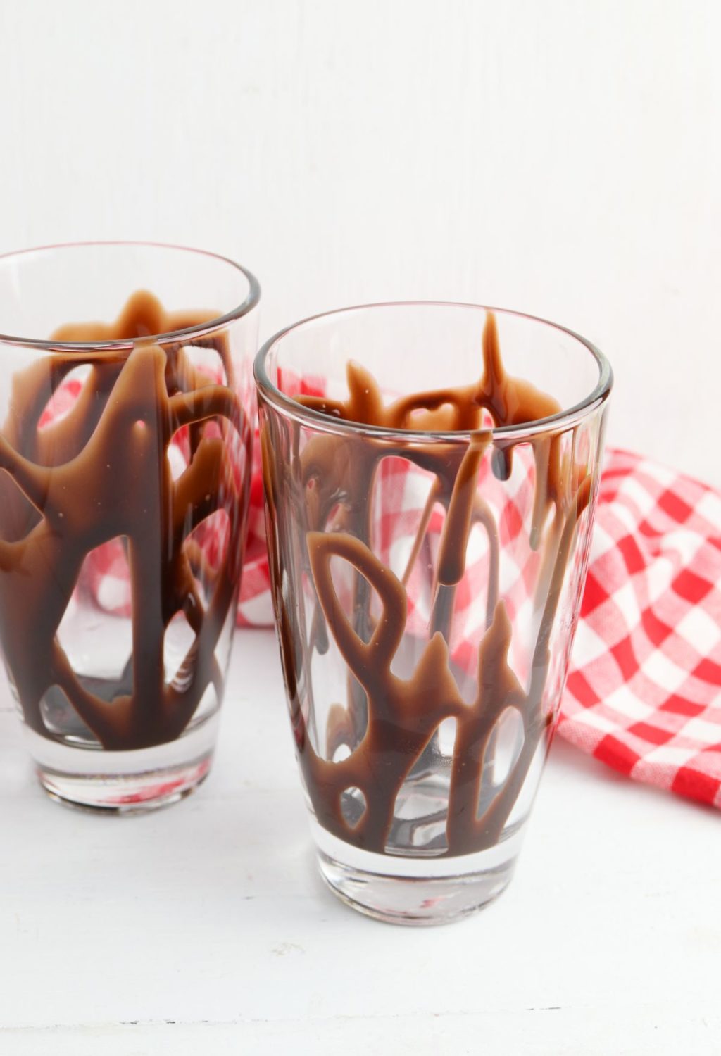 Two glasses with chocolate sauce on a red and white checkered cloth.
