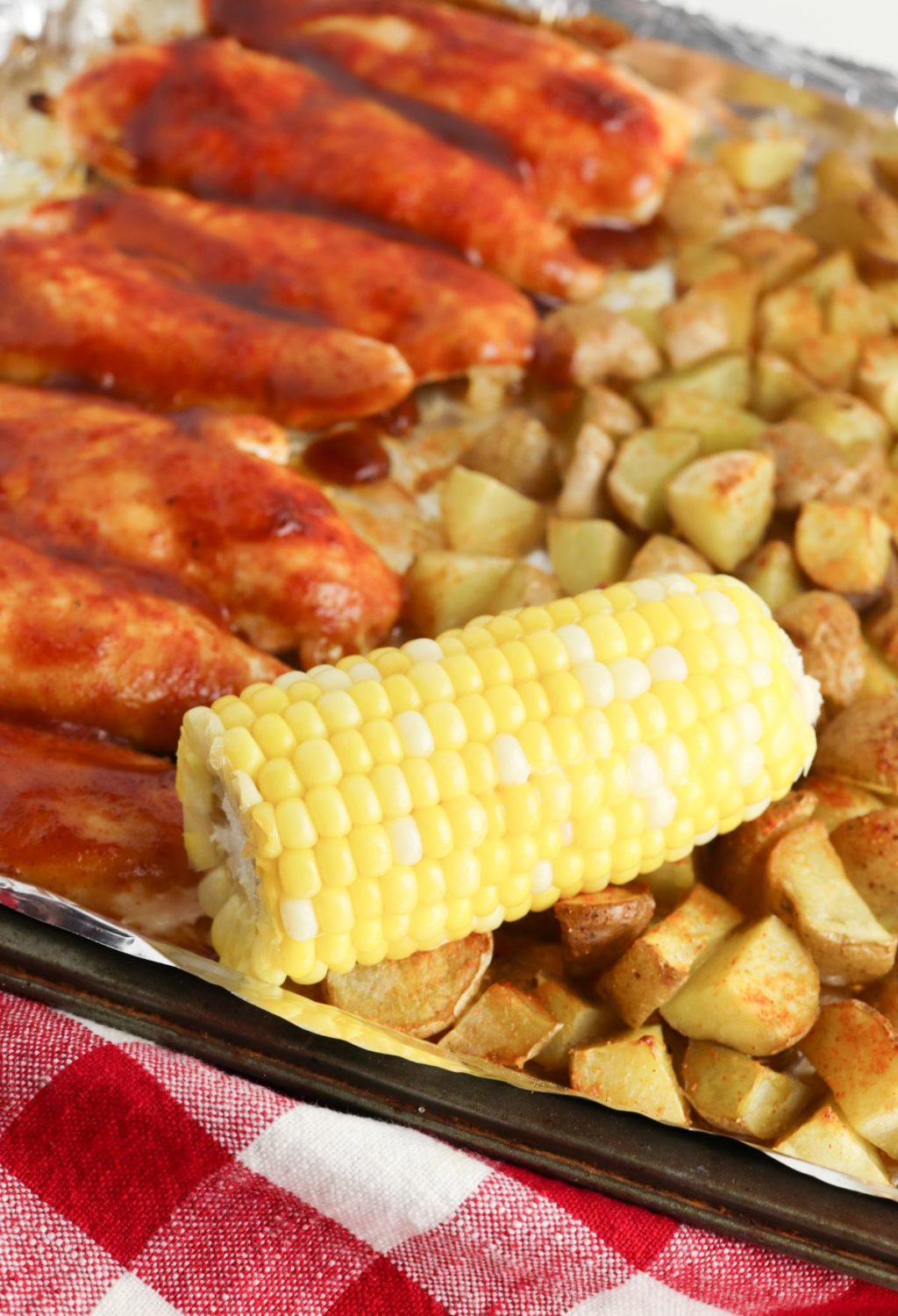 Bbq chicken and corn on a baking sheet.