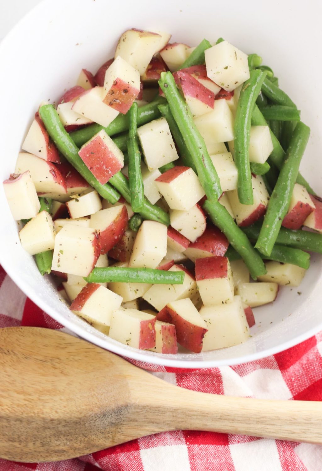Potatoes and green beans in a white bowl with a wooden spoon.