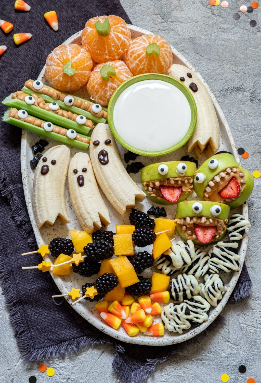 A plate of halloween snacks with bananas, apples, and oranges.