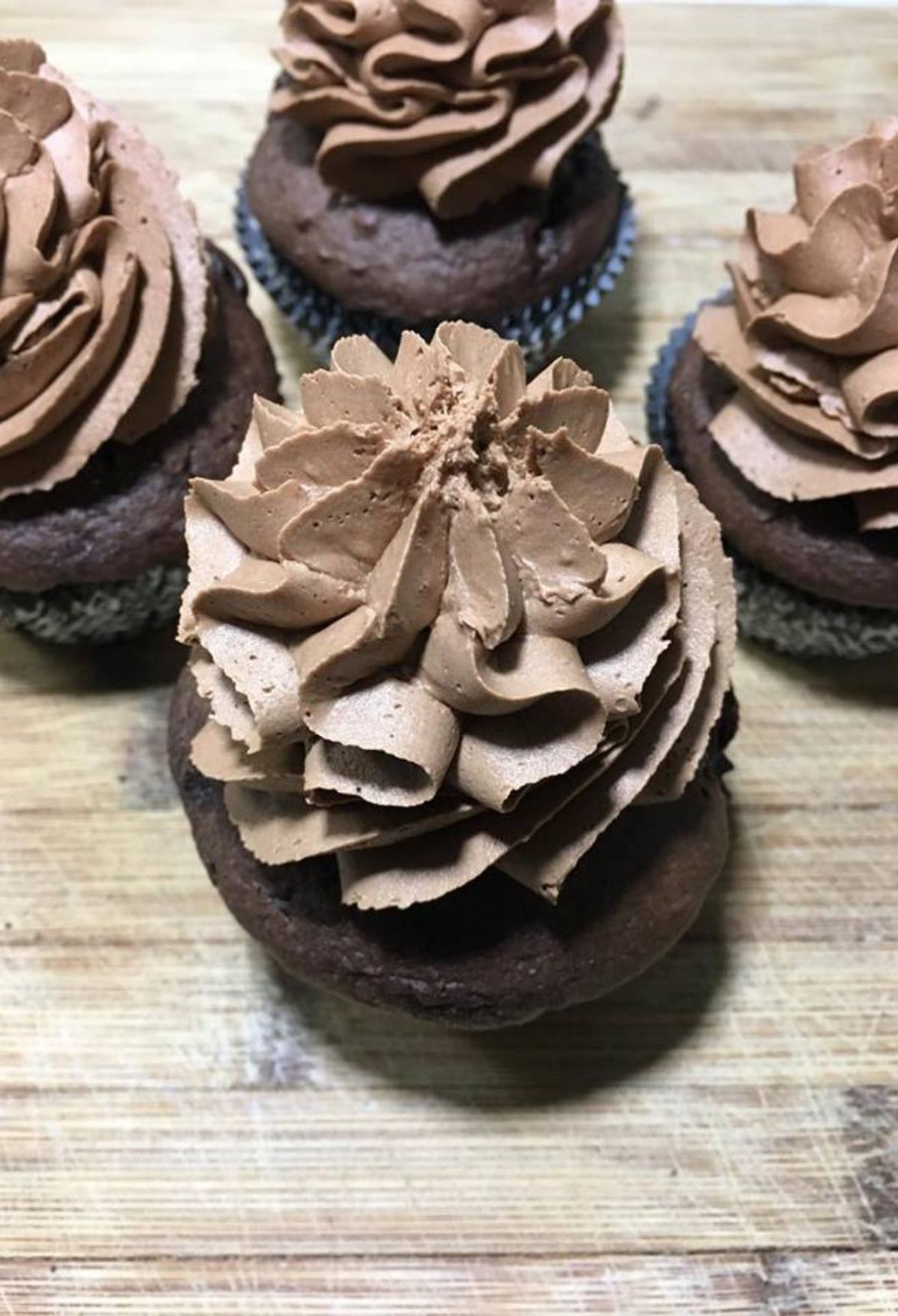 Chocolate cupcakes with chocolate frosting on a wooden cutting board.