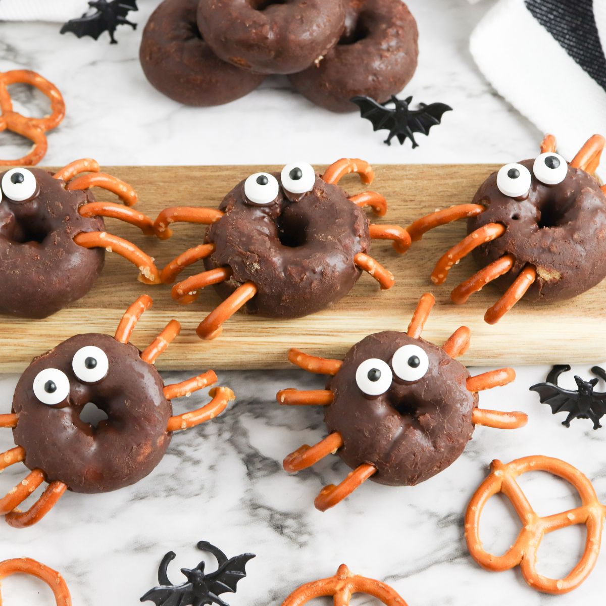 Chocolate spider donuts with pretzels on a cutting board.