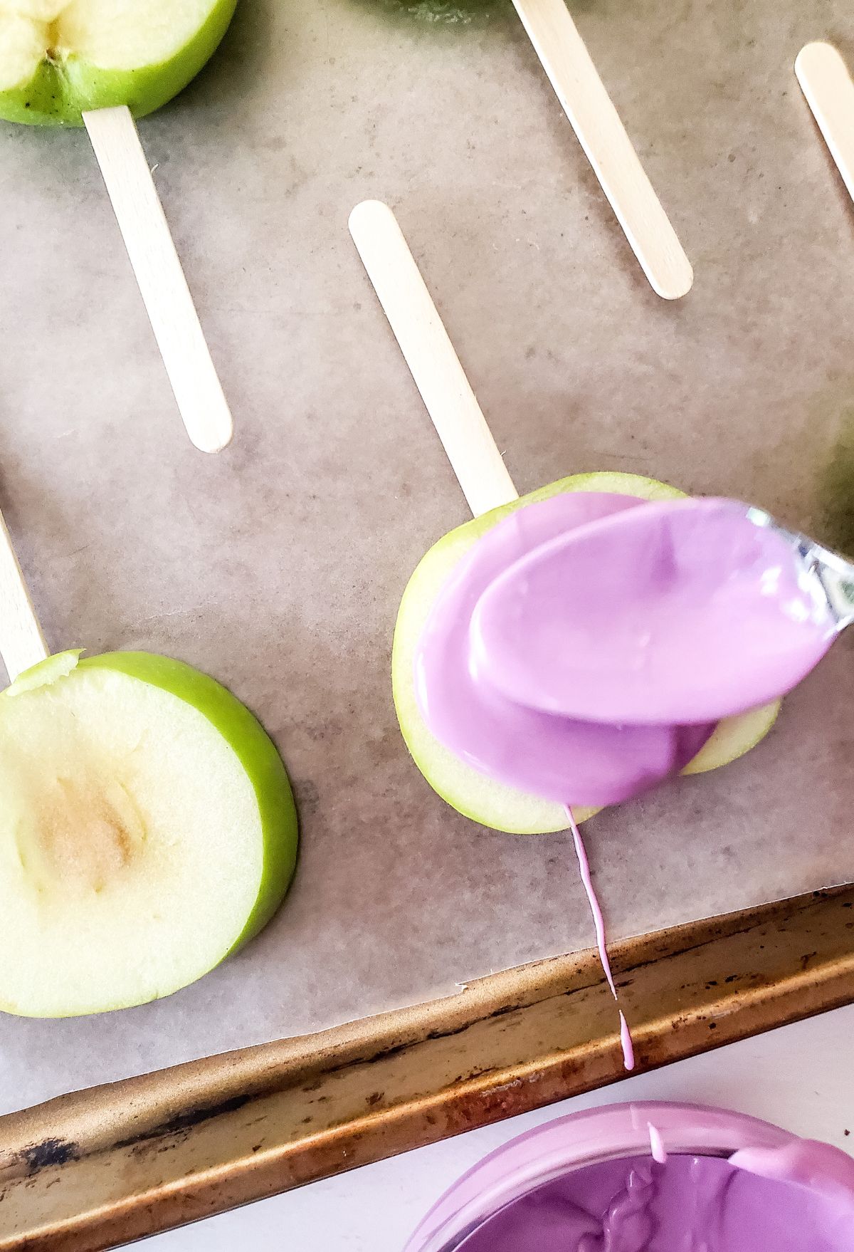 Apple popsicles with purple icing on a baking sheet.