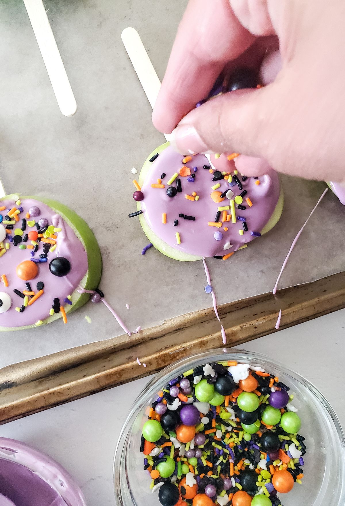 A person is putting sprinkles on a cake pop.