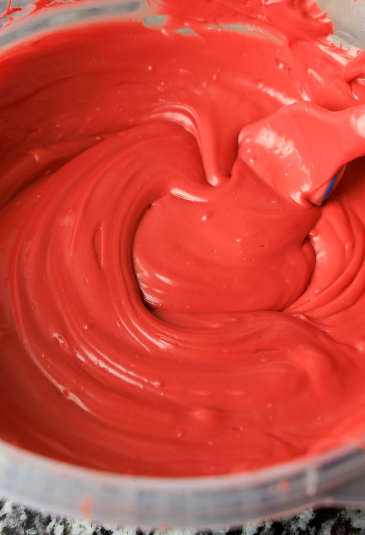 A bowl of red icing with a spoon in it.