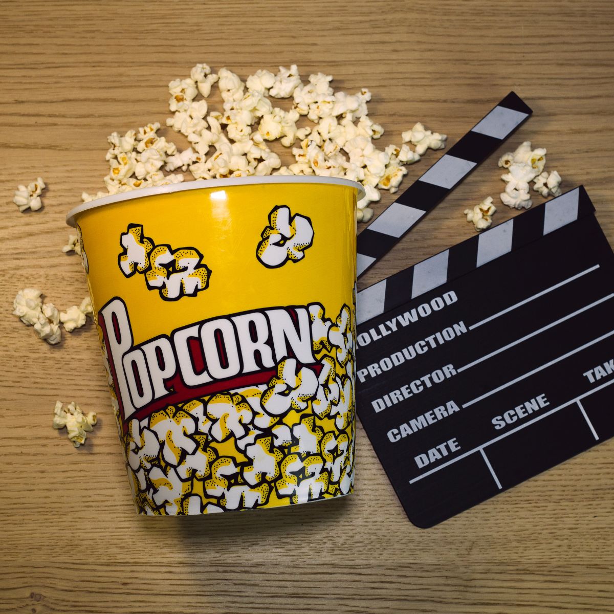 A cup of popcorn and a movie clapper on a wooden table.