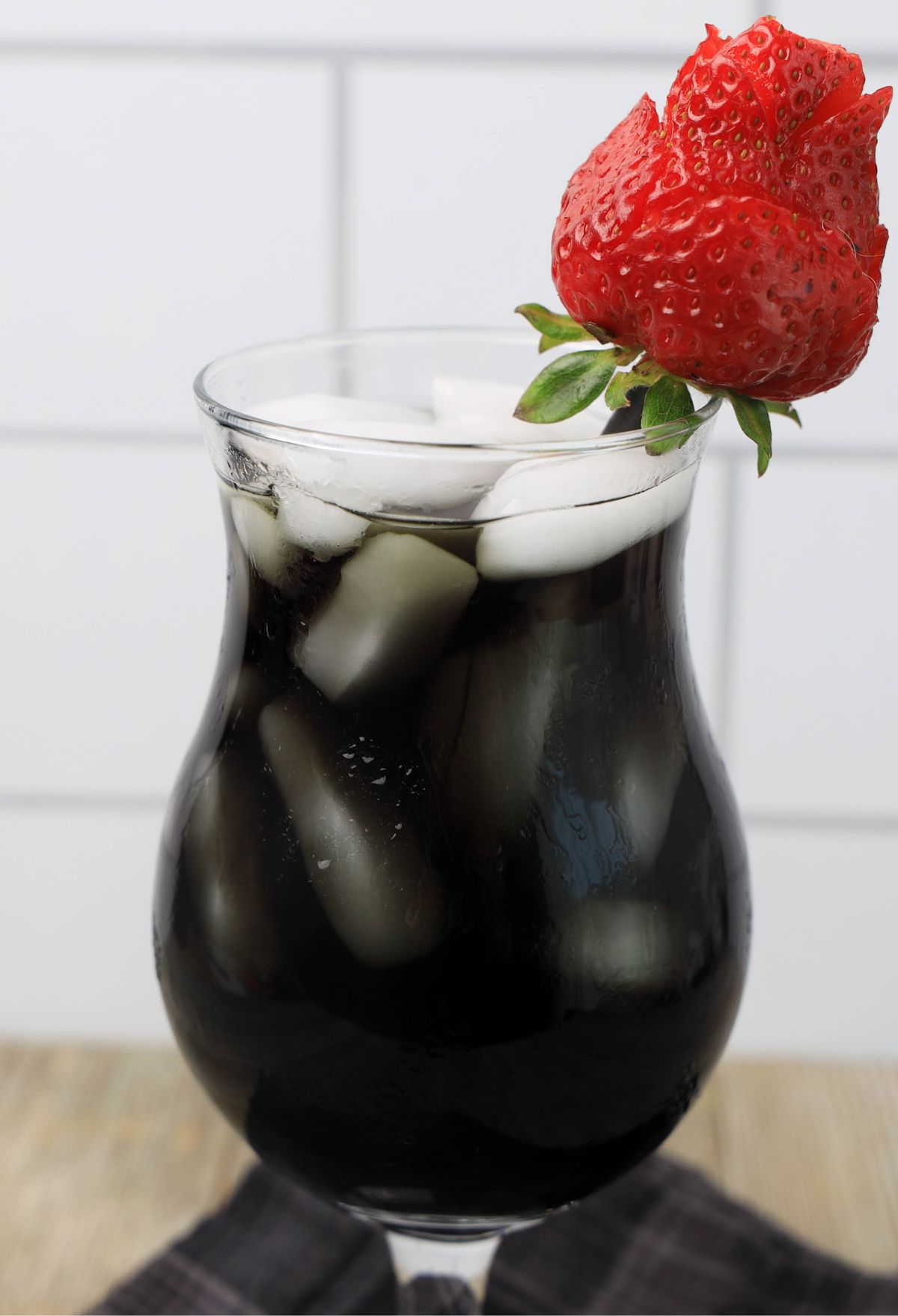 A glass of black iced tea with a strawberry on top.