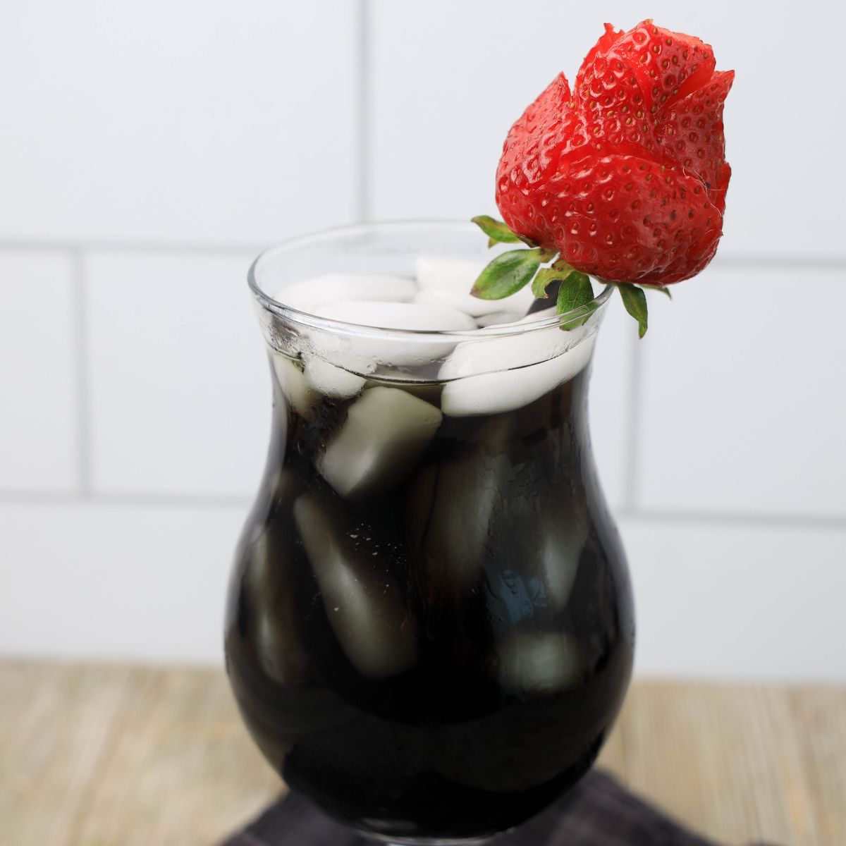 A glass of black iced tea with a strawberry on top.