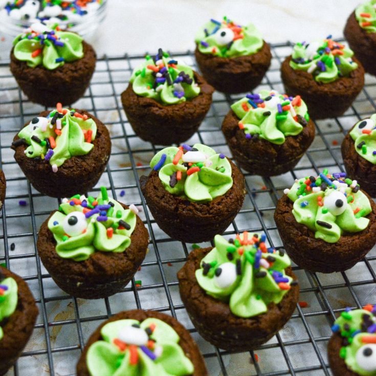Chocolate cupcakes with green frosting and sprinkles on a cooling rack.
