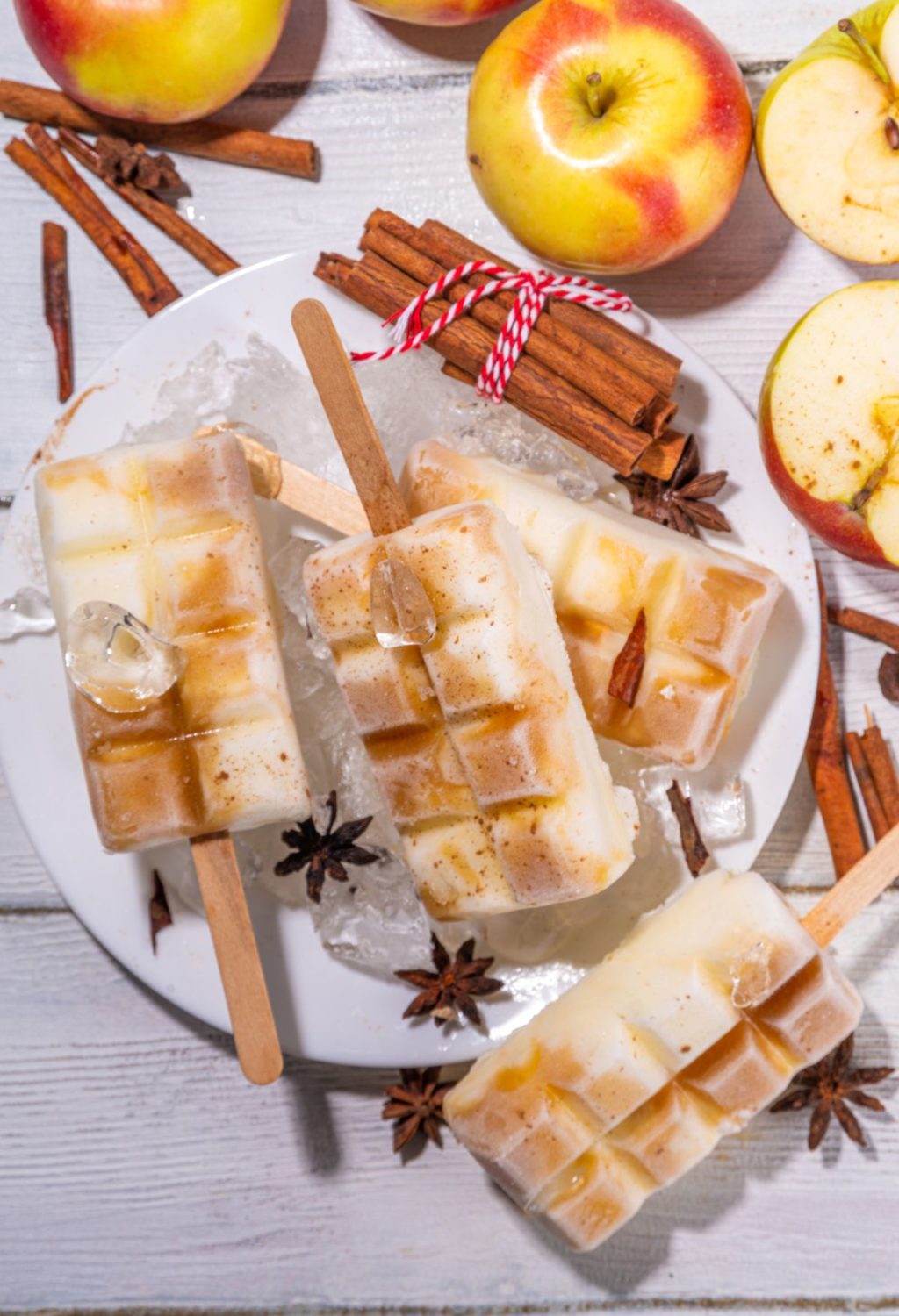 Apple popsicles on a plate with frozen apple cider and apples.