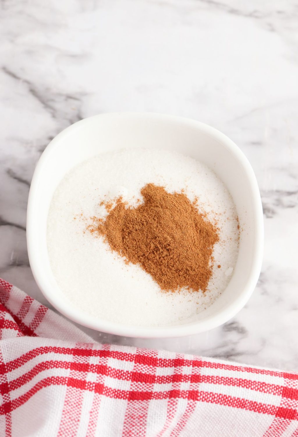 Cinnamon powder in a white bowl on a marble table.