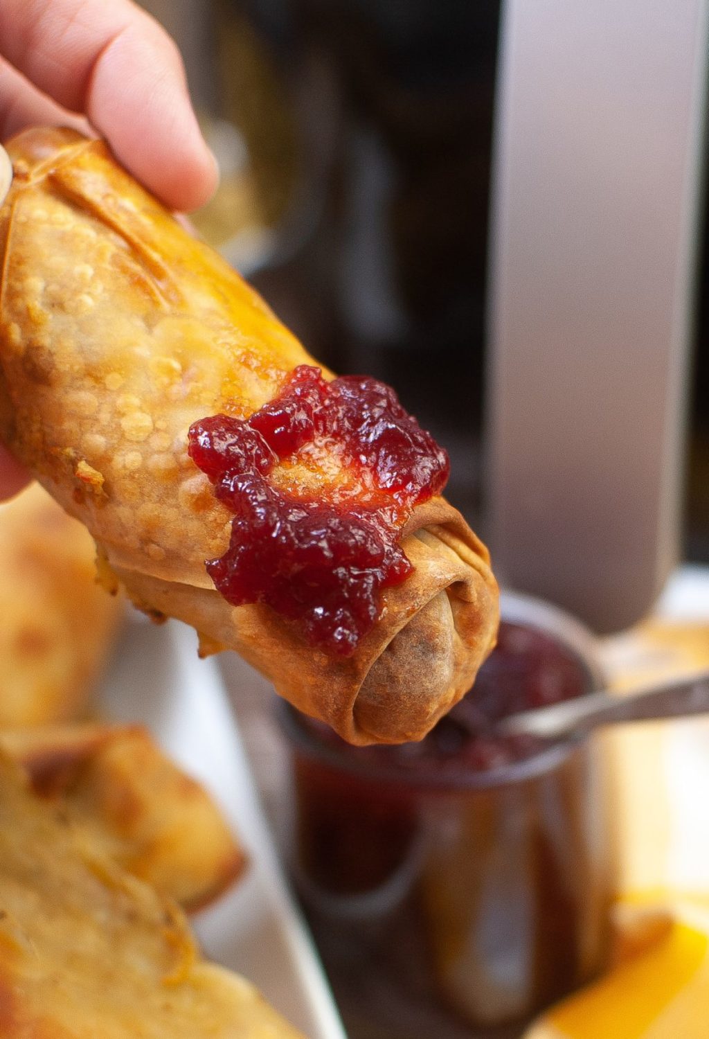 A person is holding a spring roll with jam on it.