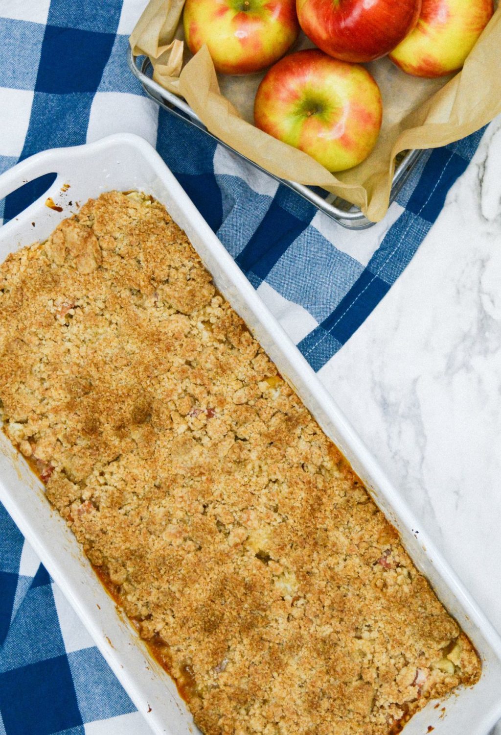 An apple crumble in a baking dish with apples next to it.