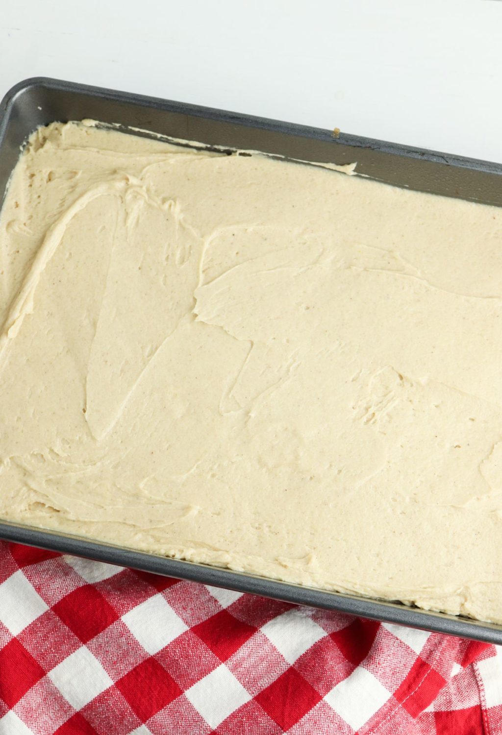 A pan with a layer of icing sitting on a red and white checkered tablecloth.