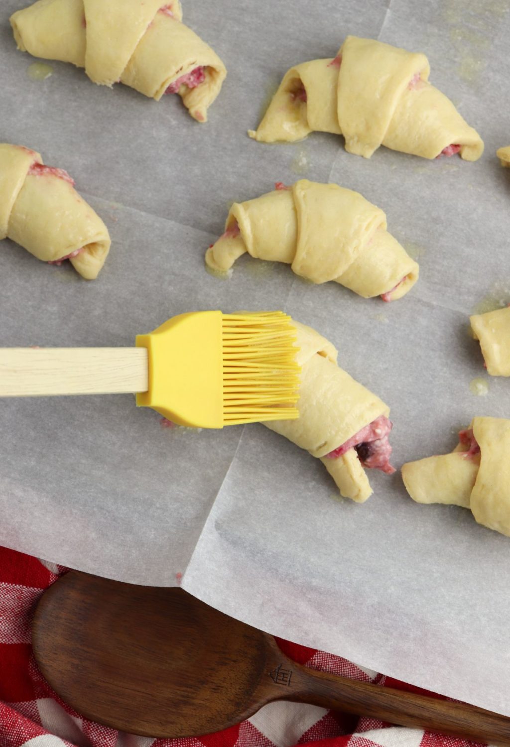 Strawberry crescent rolls on a baking sheet with a yellow spatula.