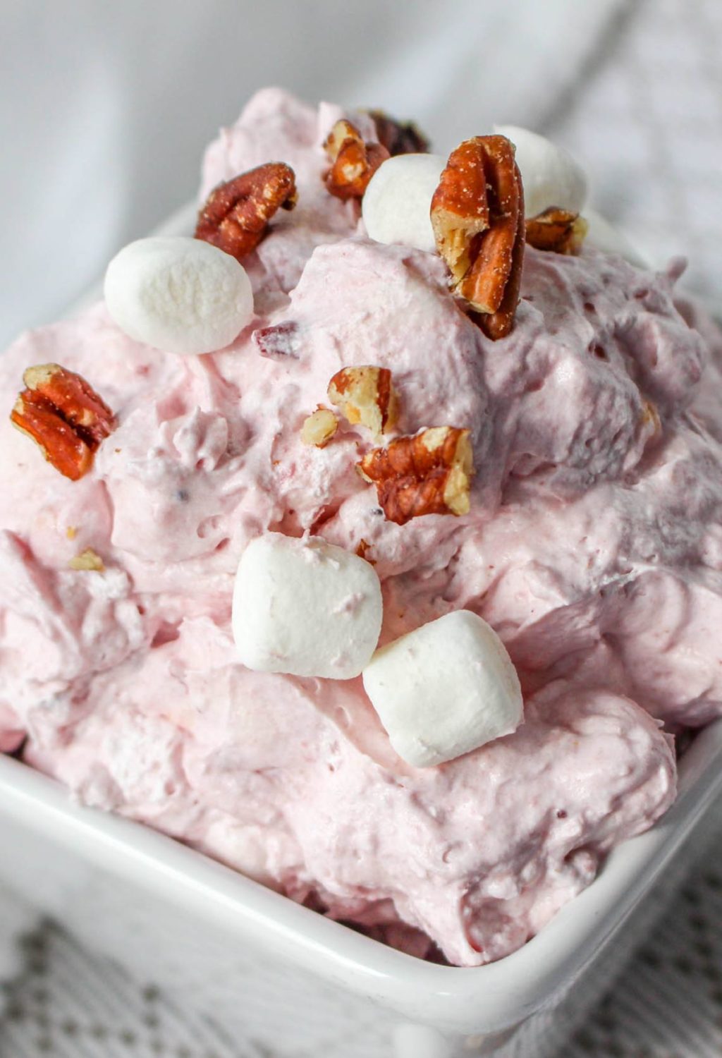Pink fluff with marshmallows and pecans in a white bowl.