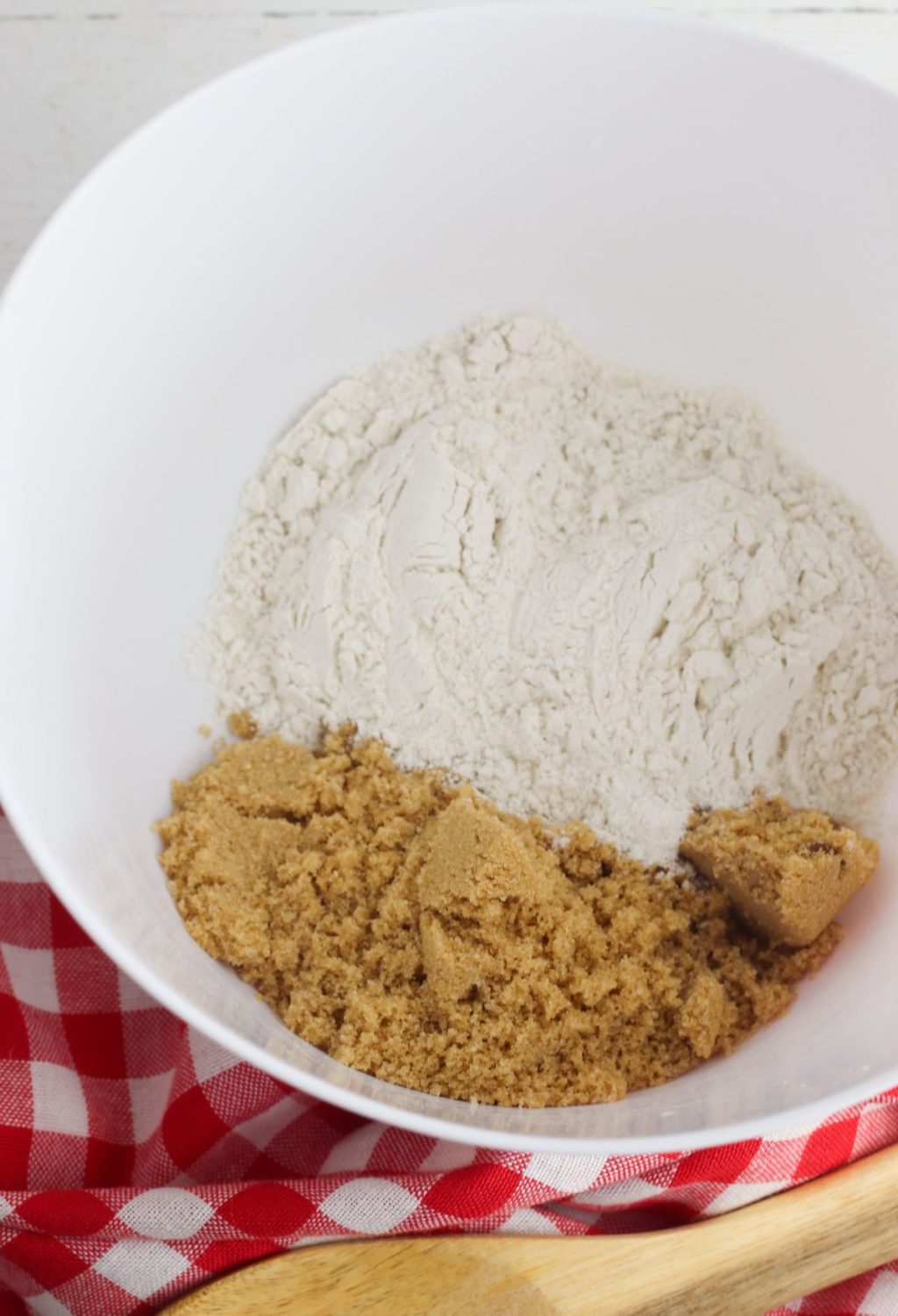 A white bowl with flour, sugar and a wooden spoon.
