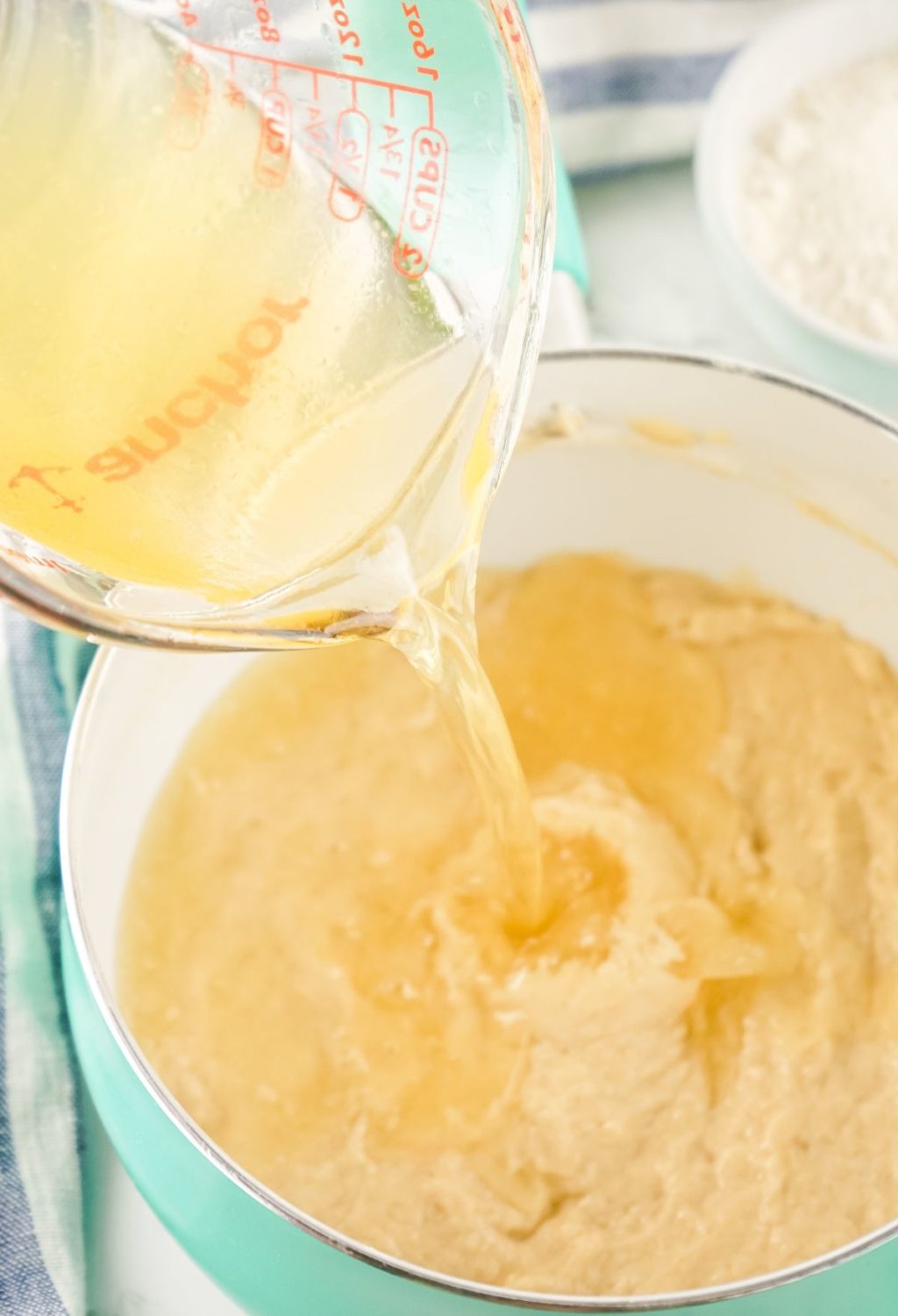 A yellow liquid is being poured into a bowl of batter.