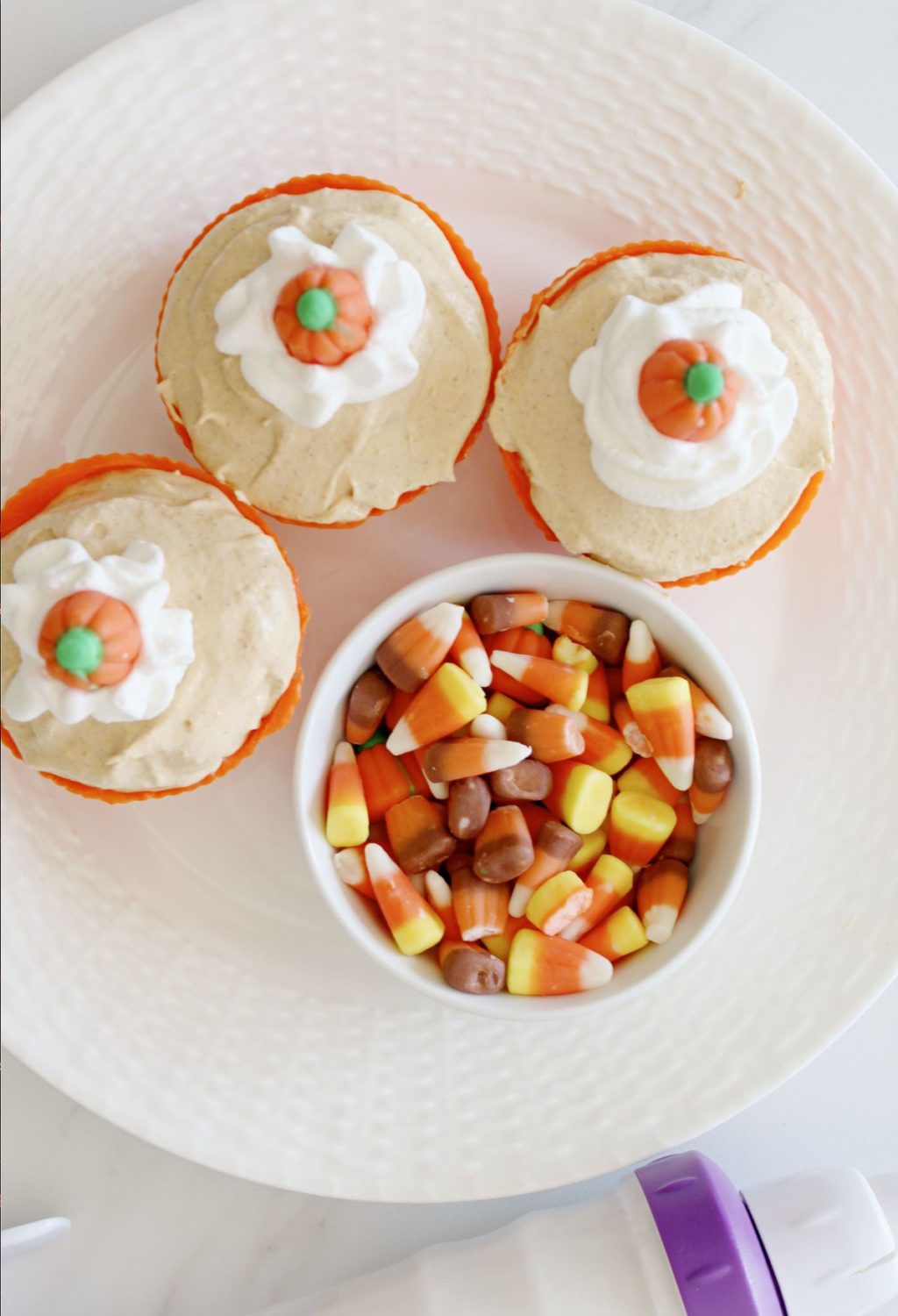 Three pumpkin cupcakes on a plate with candy corn.