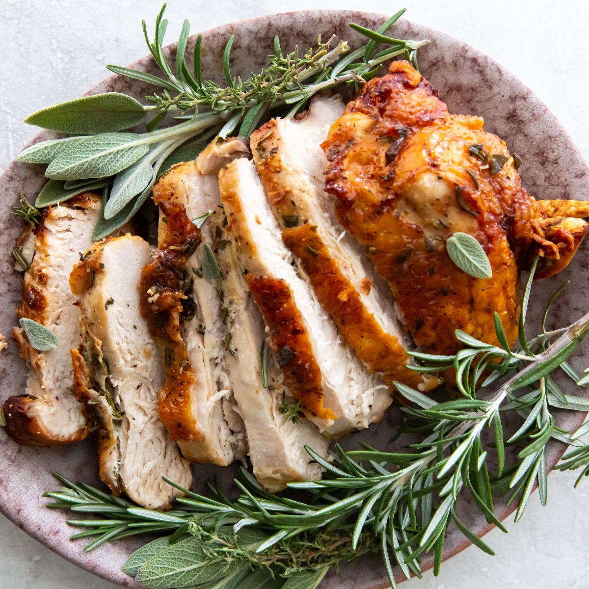 Sliced chicken breast with rosemary sprigs on a plate.