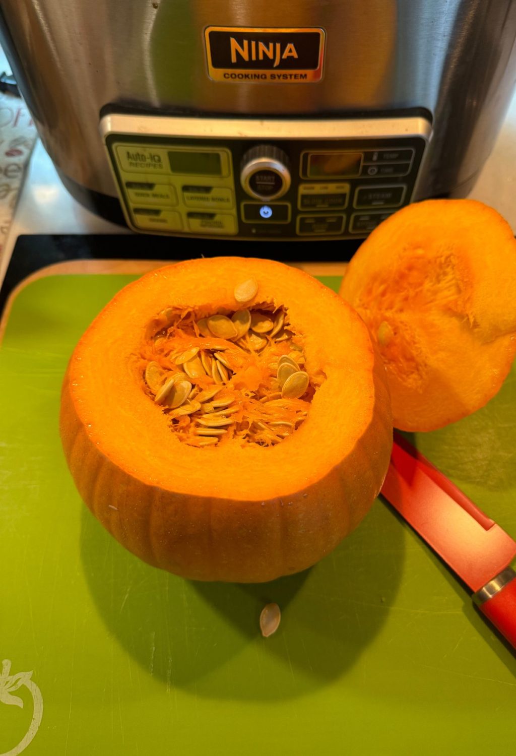 A pumpkin on a cutting board next to an instant pot.