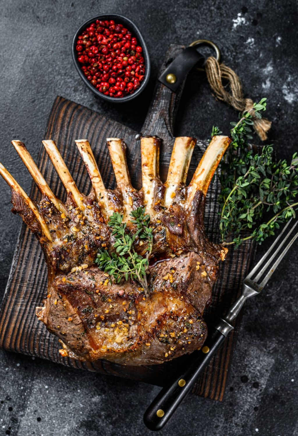 A rack of lamb with herbs and spices on a wooden cutting board.