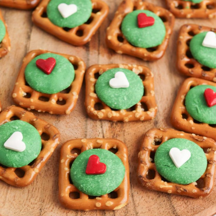 Christmas pretzels with green hearts on a wooden cutting board.