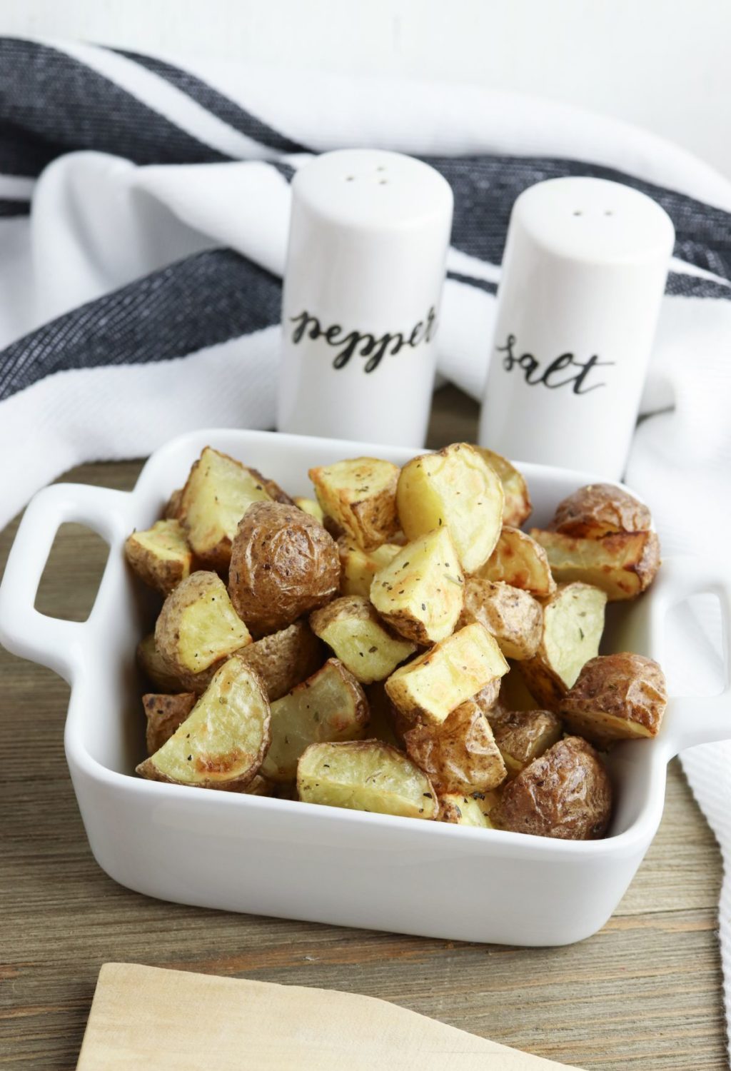 Roasted potatoes in a white dish with salt and pepper shakers.