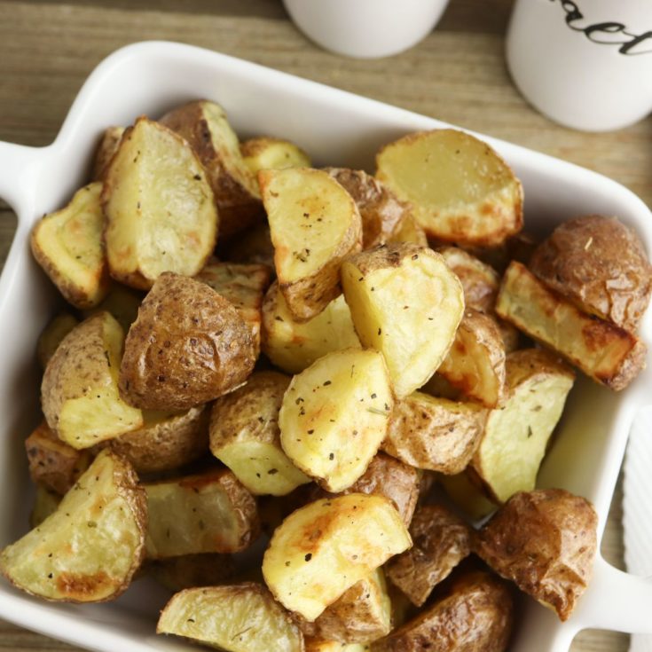 Roasted potatoes in a white dish with a cup of coffee.