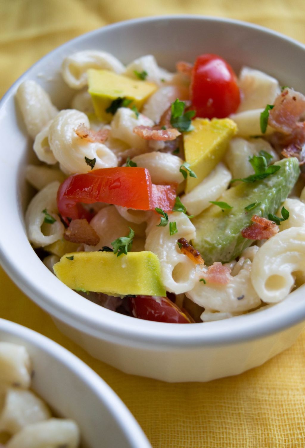 A bowl of pasta with avocado, tomatoes and bacon.