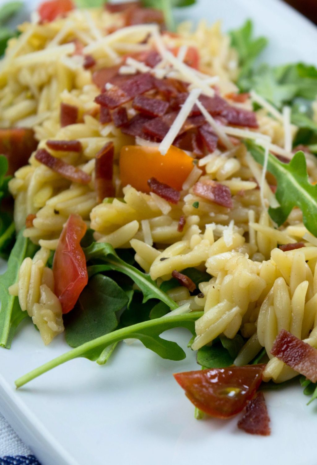 A plate with arugula, tomatoes, bacon and orzo.