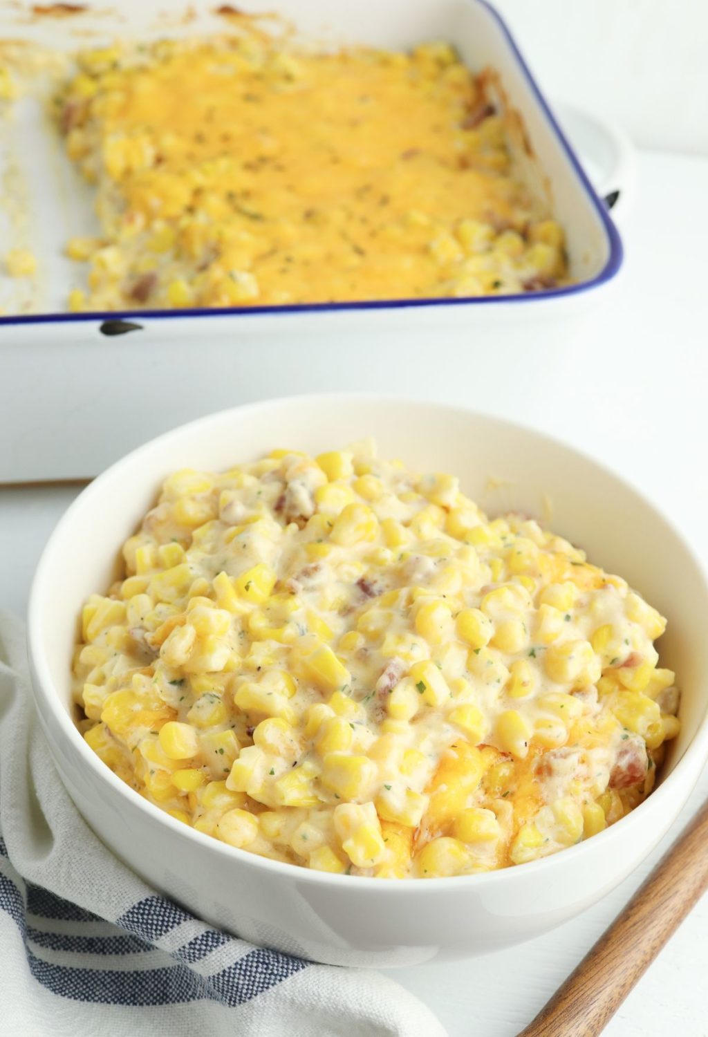 A bowl of cheesy corn casserole on a white table.