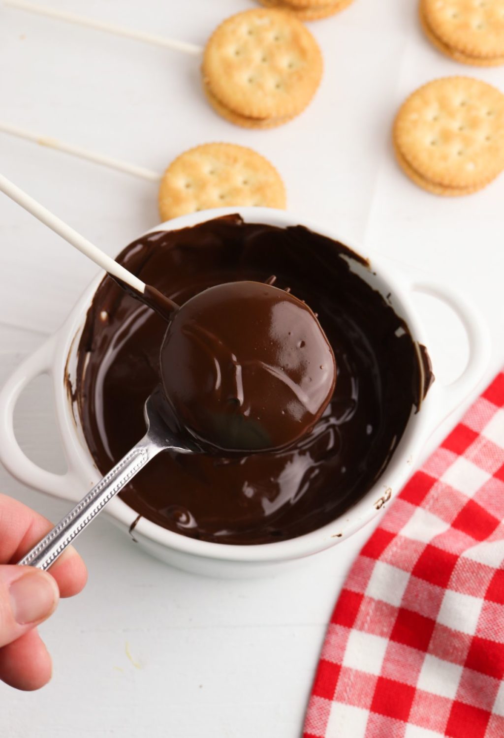 A person is holding a spoon and dipping a cracker in chocolate.