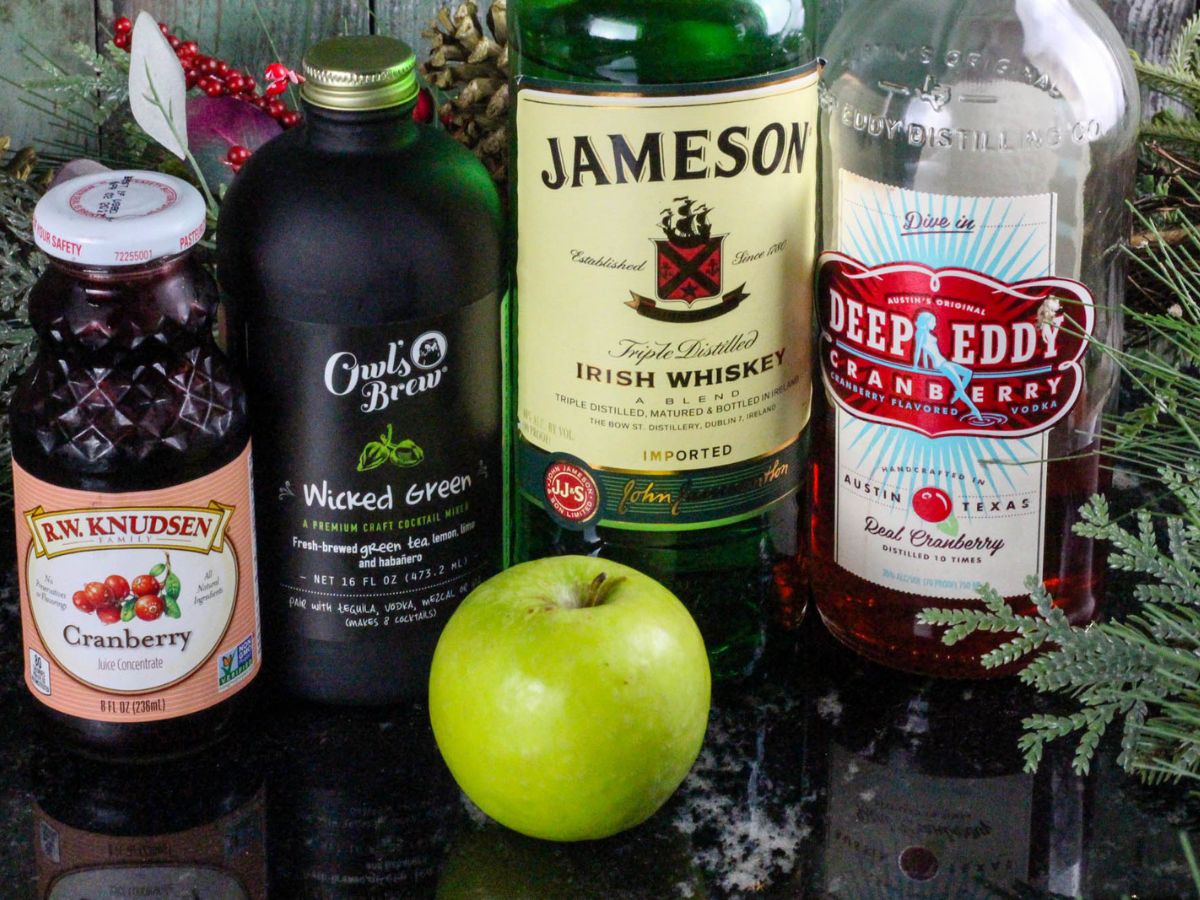 A bottle of jameson gin, an apple, and a bottle of cranberry juice.