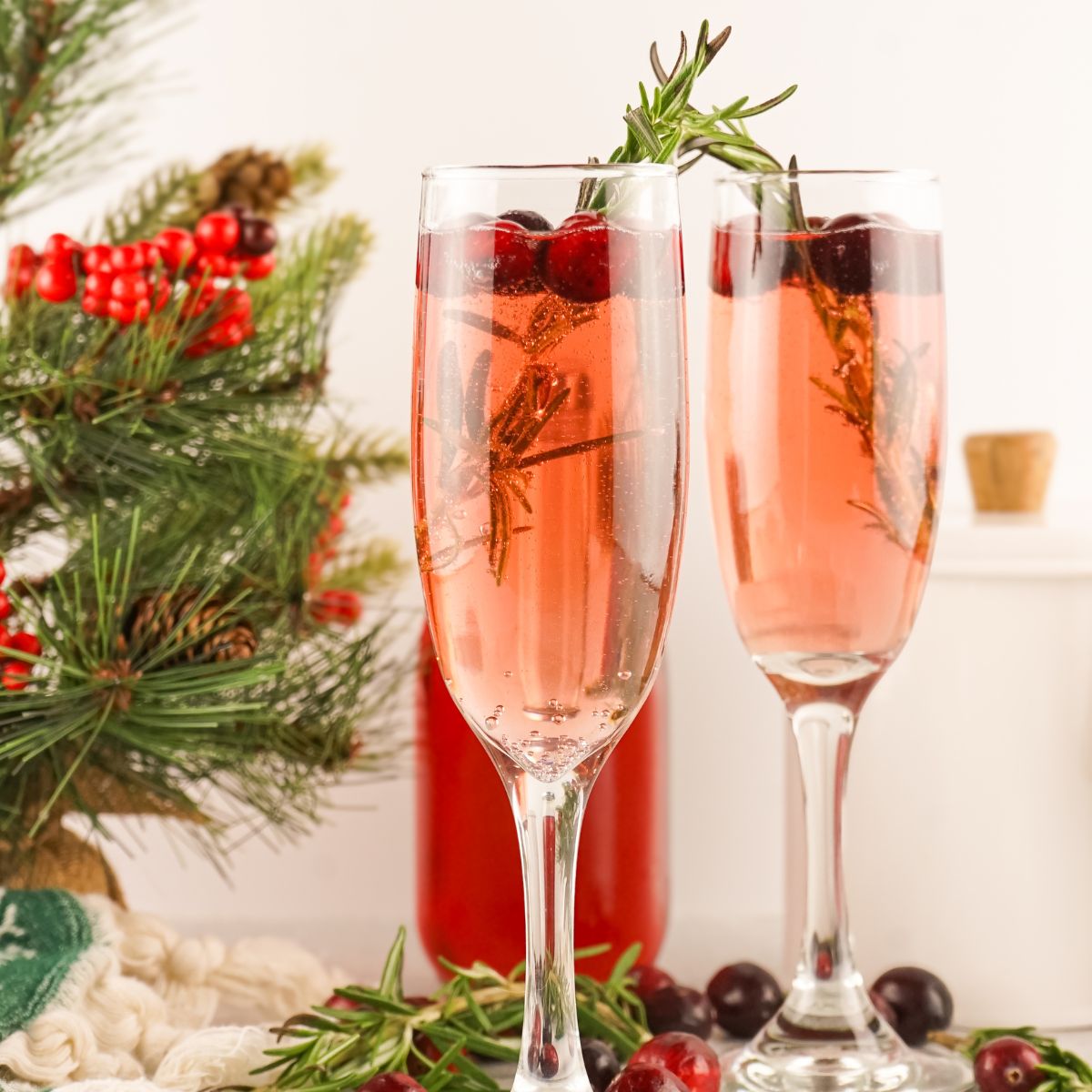 Two glasses of champagne with cranberries and sprigs of rosemary.