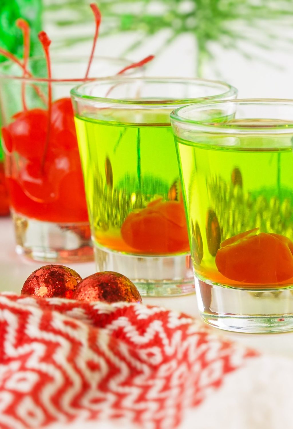 Two glasses of green liquid with cherries on a table.
