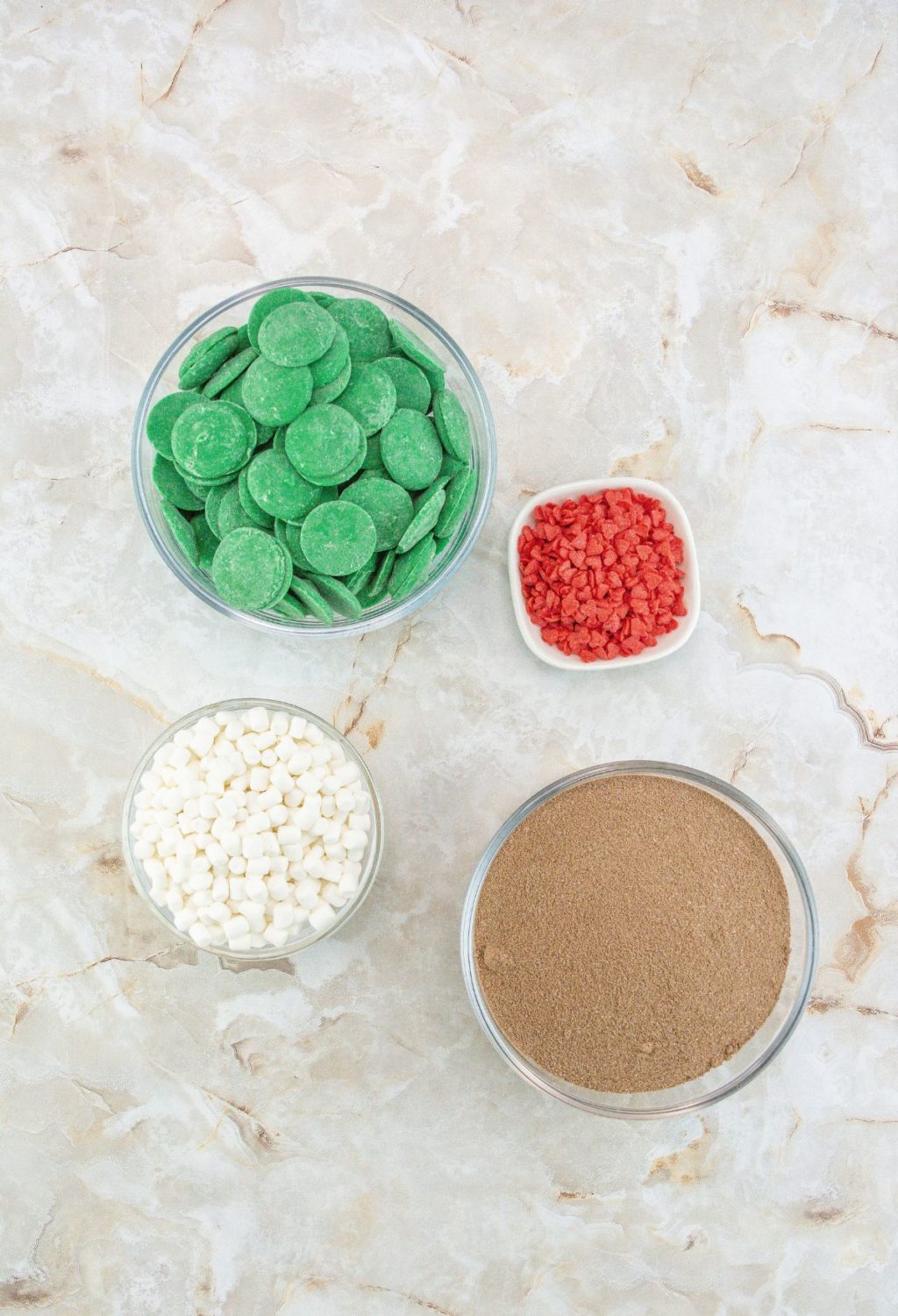 A bowl of green, red, and white sprinkles on a marble table.