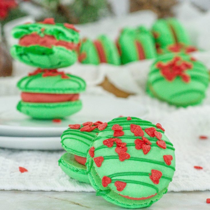 A plate of green and red macarons on a white plate.