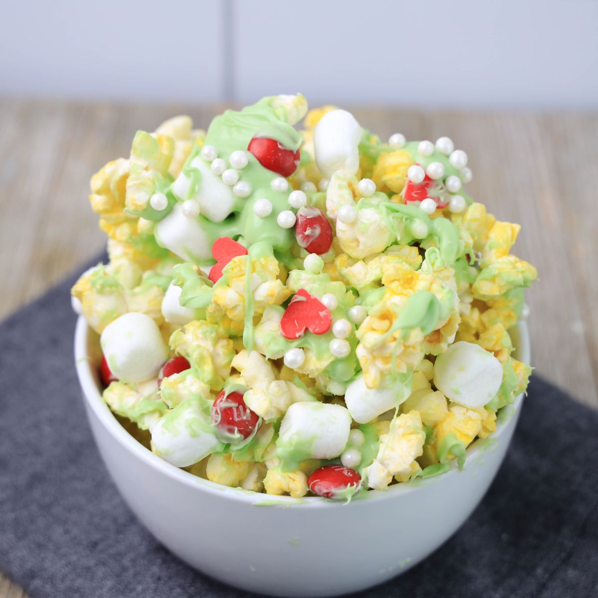 A bowl of popcorn with green icing and marshmallows.
