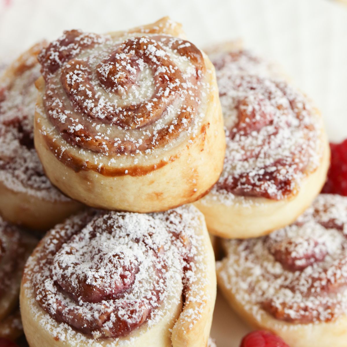 A stack of raspberry cinnamon rolls on a plate.