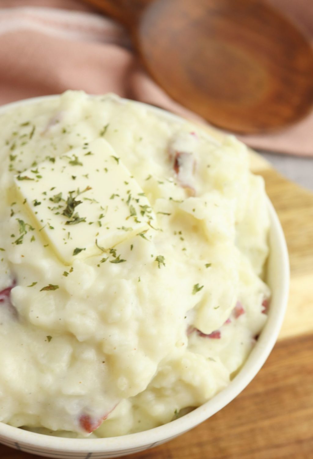 A bowl of mashed potatoes on a wooden cutting board.