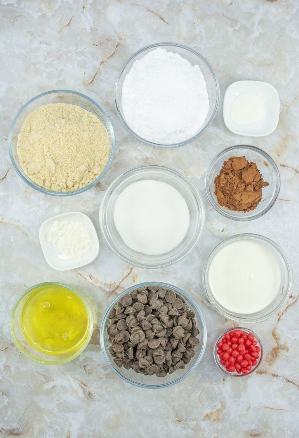 Ingredients for a chocolate cake in bowls on a marble surface.