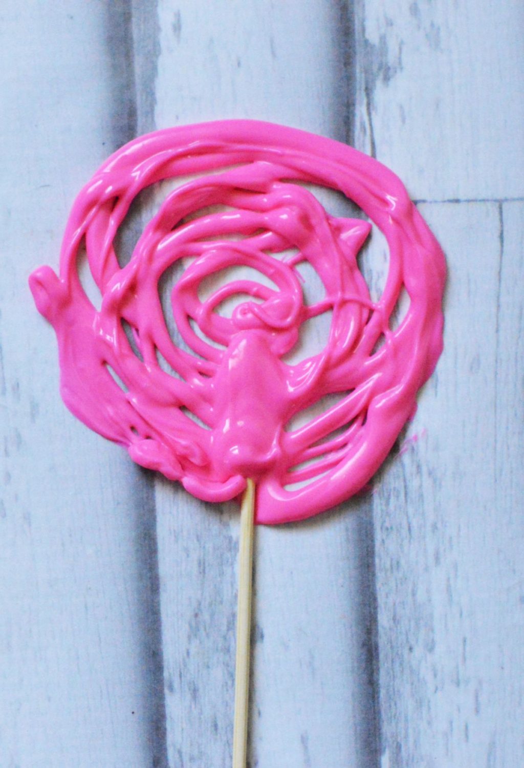 A pink lollipop on a wooden stick.