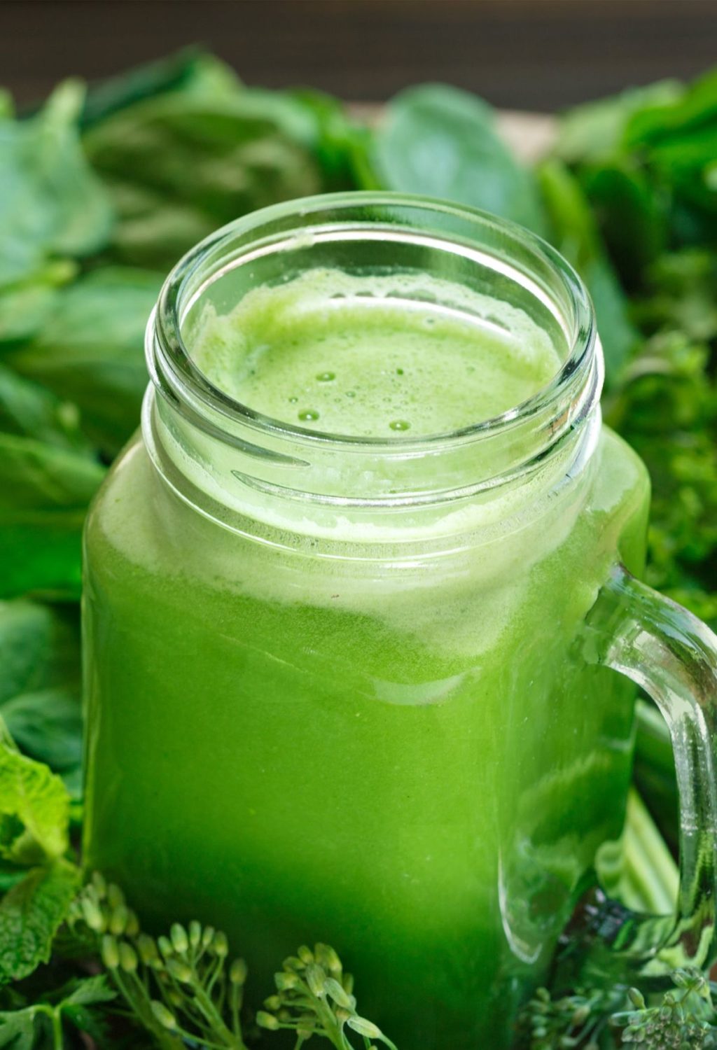 A jar of green juice surrounded by green leaves.