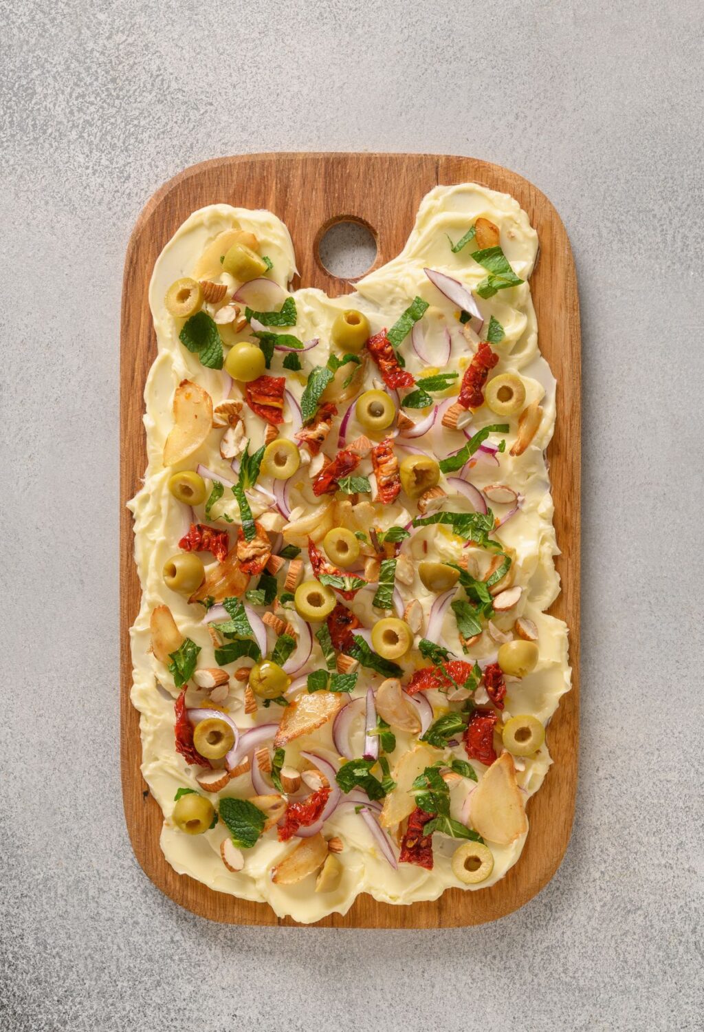 A pizza with olives and onions on a wooden cutting board generously sprinkled with melted butter.