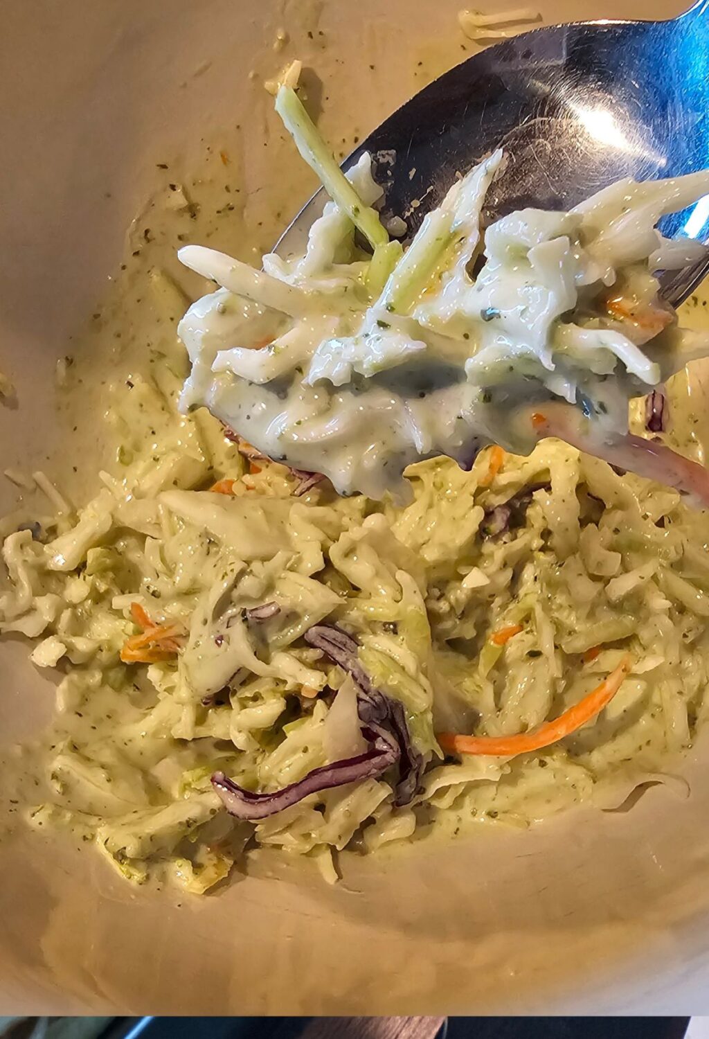 A bowl of coleslaw with a spoon in it.