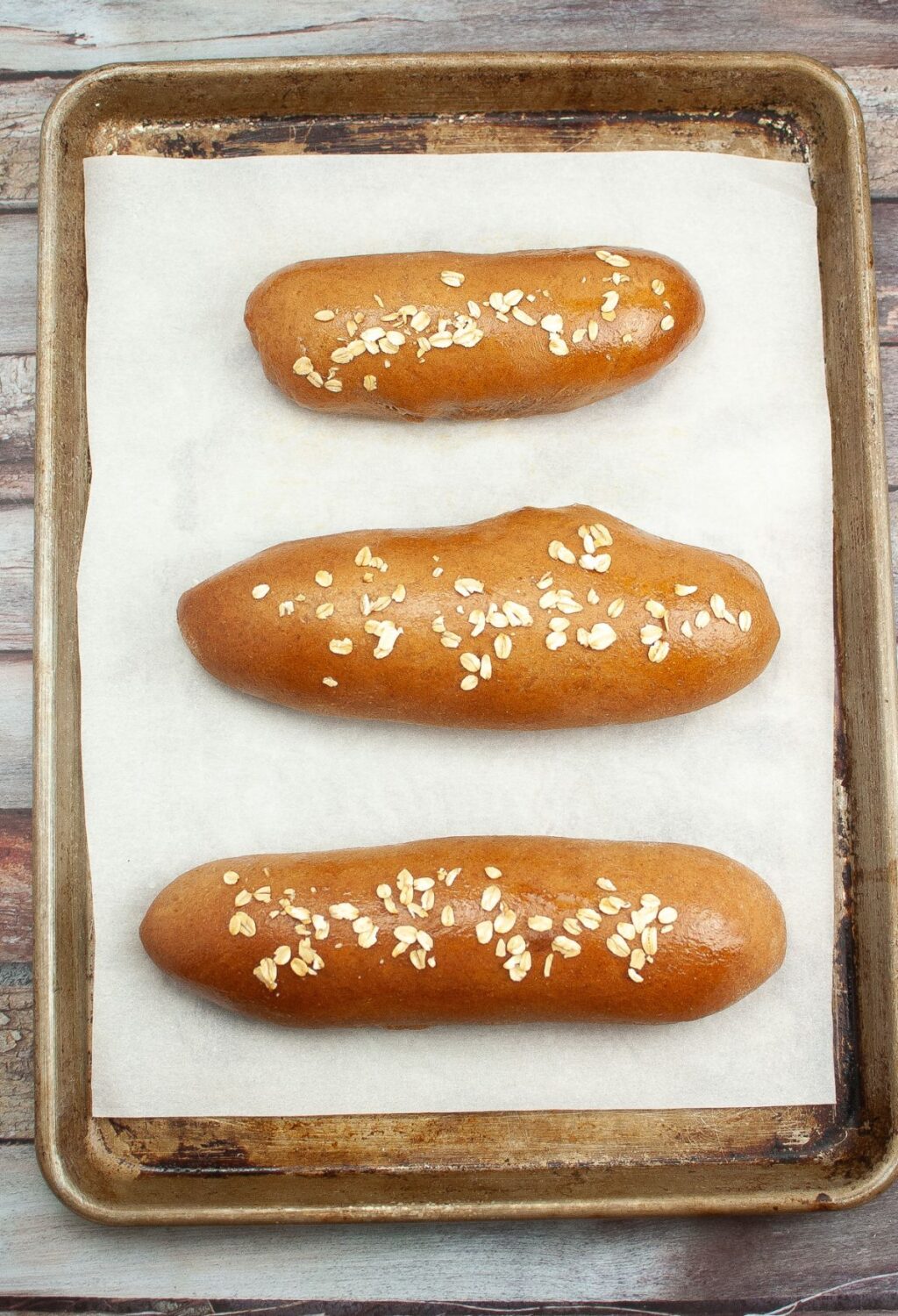 Three hot dogs on a baking sheet with oats on top.